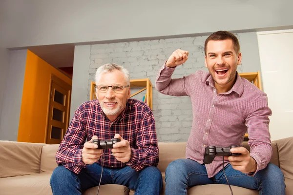 Отец и сын сидят на диване и играют в видеоигры — стоковое фото
