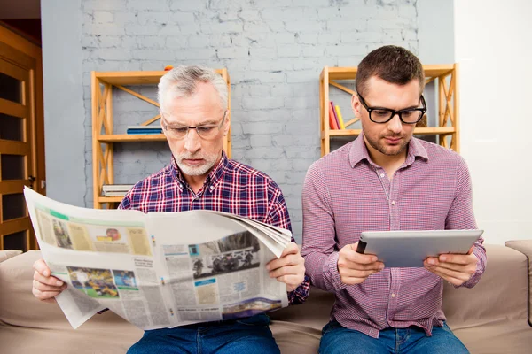 Stary ojciec czytając gazety i jego syna za pomocą tabletu — Zdjęcie stockowe