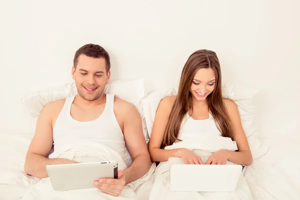 Man and woman lying in bed and working with laptop and tablet — Stock Photo, Image