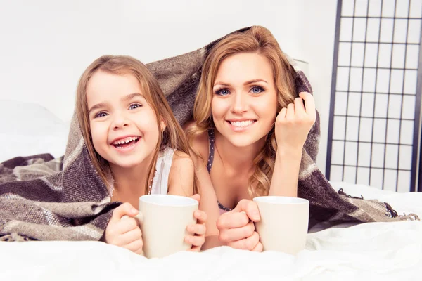 Portrait de fille heureuse et mère couchée sous plaid avec tasse — Photo