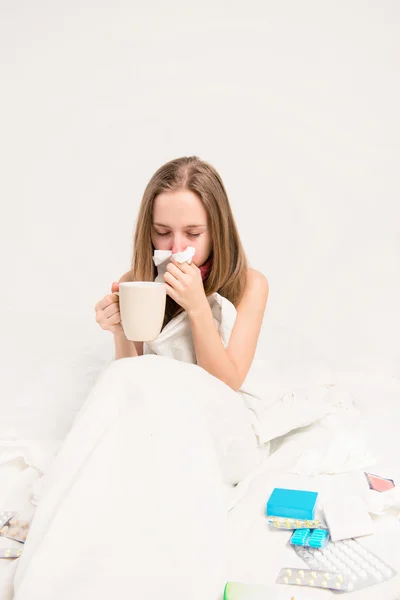 Sjuk kvinna med rheum sitter i sängen och hålla en kopp te — Stockfoto