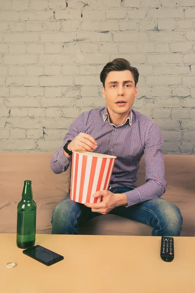 Guapo joven comiendo palomitas de maíz y viendo la televisión — Foto de Stock