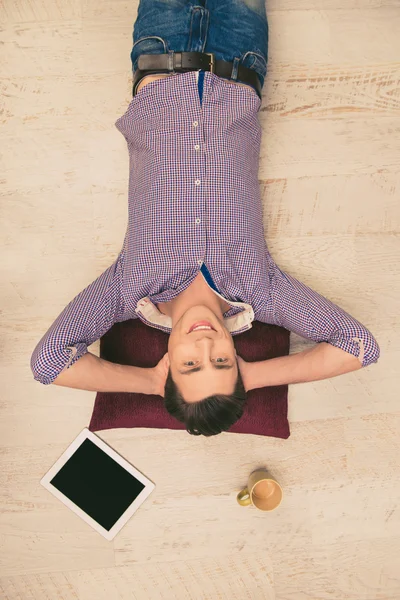 Vista superior de la foto del hombre sonriente acostado en el suelo con la taza y ta — Foto de Stock