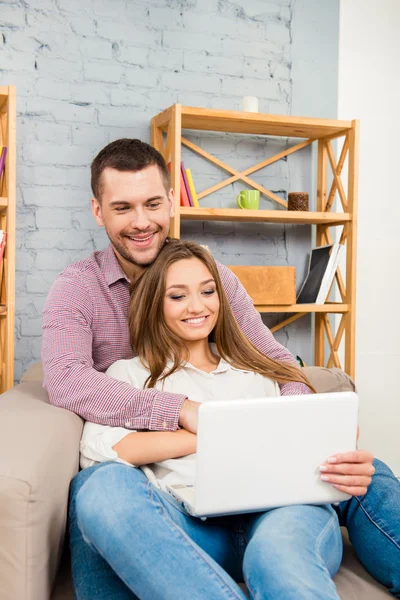 Handsome man embracing his girlfriend sitting on sofa with lapto — Stock Photo, Image