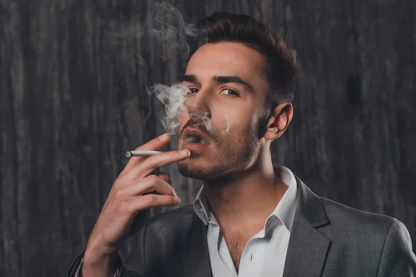 Красивый жестокий мужчина в сером костюме курит сигарету — стоковое фото