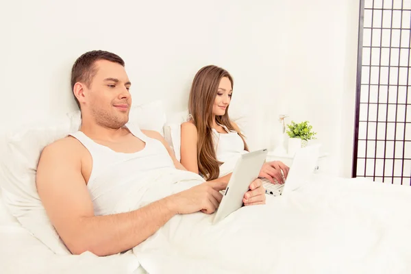 Portrait of young family working in bed with tablet and laptop — Stock Photo, Image