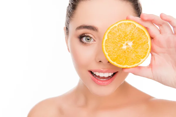 Mujer sonriente ocultando el ojo detrás de la mitad de naranja — Foto de Stock