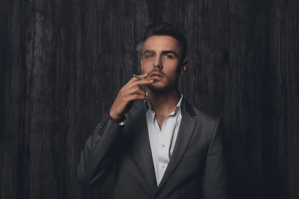 Sexy hombre brutal en traje gris fumando un cigarrillo —  Fotos de Stock