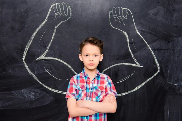 Little boy on backgroung of blackboard with drawn muscles — Stock Photo, Image