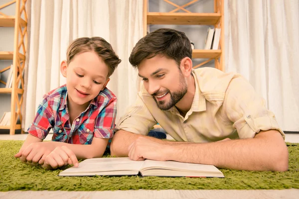 Ojciec i jego synek, leżąc na dywanie i czytanie książek — Zdjęcie stockowe
