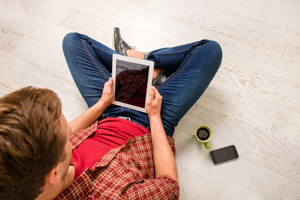 Bovenaanzicht van jonge man zittend op de vloer aan met de Tablet PC- en readin — Stockfoto