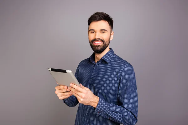 Guapo feliz empresario sosteniendo la tableta sobre fondo gris — Foto de Stock