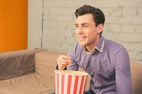 Sonriente hombre guapo con palomitas de maíz viendo interesante película — Foto de Stock