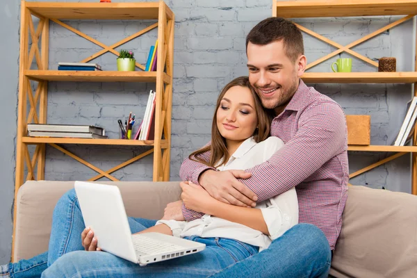 Ευτυχισμένο ζευγάρι στην αγάπη που κάθεται στον καναπέ με το laptop και κάνει s — Φωτογραφία Αρχείου