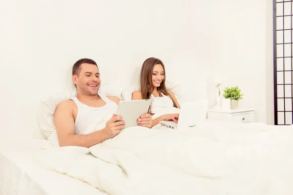 Cheerful man reading news on tablet and his wife working on lapt — Stock Photo, Image