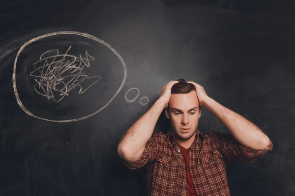 Young tired man at a loss on the background of chalkboard — Stock Photo, Image