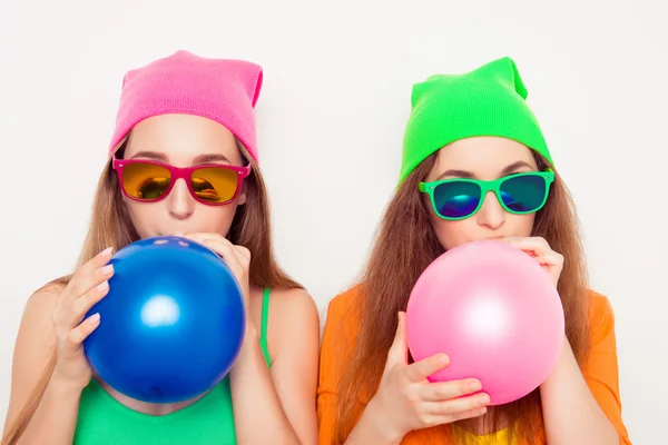 Porträtt av två flickor i hattar och glasögon blåser ballonger — Stockfoto