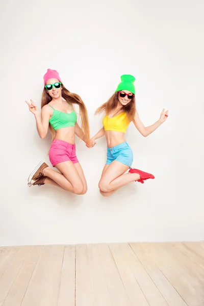 Two happy hipster women in hats and glasses jumping — Stock Photo, Image