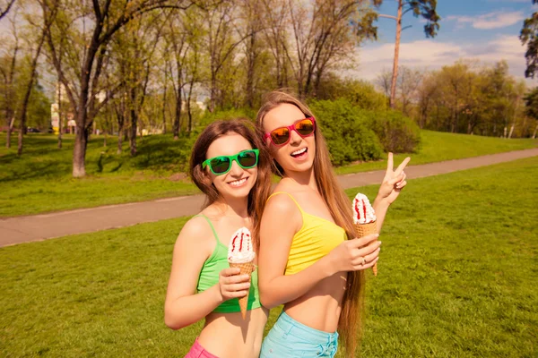 Duas irmãs sorridentes de óculos comendo sorvete no parque — Fotografia de Stock