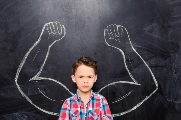 Portrait of  boy on backgroung of blackboard with drawn muscles — Stock Photo, Image