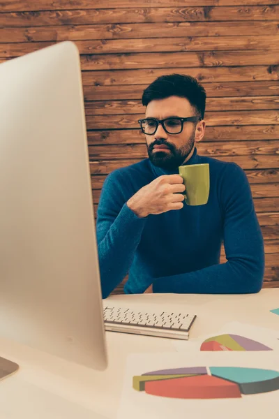 Young businessman in glasses drinking coffee while working on pc — Stock Photo, Image