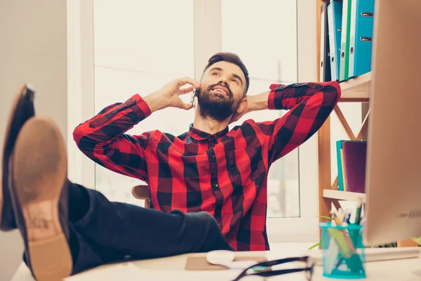 Hombre feliz hablando por teléfono y sosteniendo las piernas en la mesa — Foto de Stock