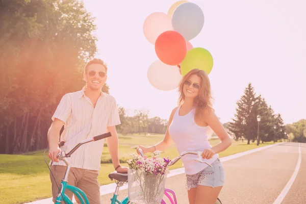 Jovem e mulher tendo fim de semana com bicicleta e balões — Fotografia de Stock