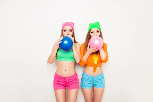 Two hipster girls preparing for party and blowing balloons — Stock Photo, Image