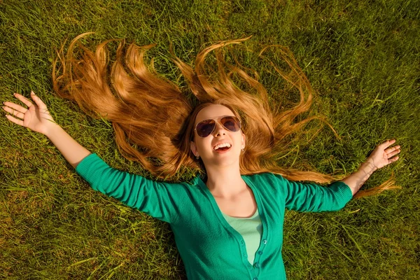 Happy cheerful long-haired girl in spectacles lying on lawn — Stock Photo, Image