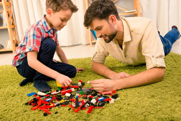 Padre e hijo jugando con el constructor mientras están acostados en la alfombra — Foto de Stock