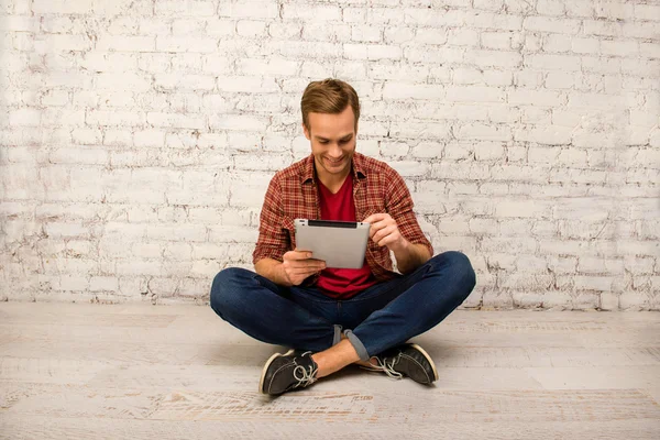 Gelukkig man zittend op de vloer met gekruiste benen en tablet — Stockfoto