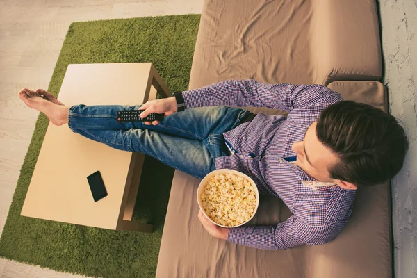 Vista superior del hombre sentado en casa y viendo películas con palomitas de maíz — Foto de Stock