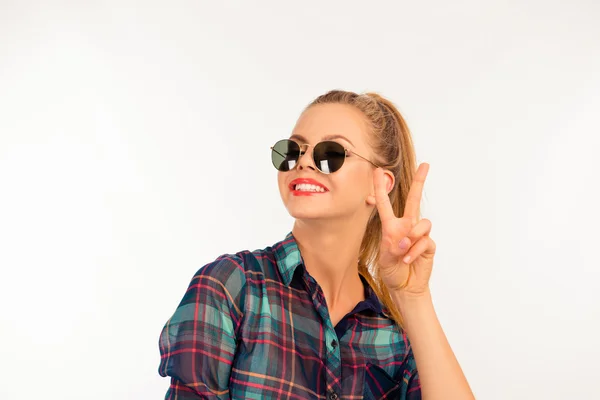 Söt flicka i en rutig skjorta med solglasögon visar två finge — Stockfoto