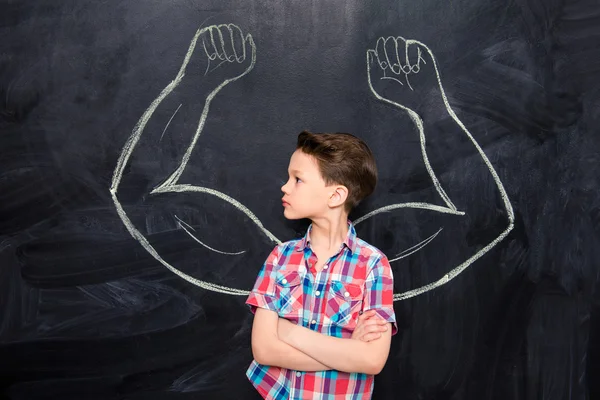 Liten pojke tittar på muskler dras på blackboard — Stockfoto