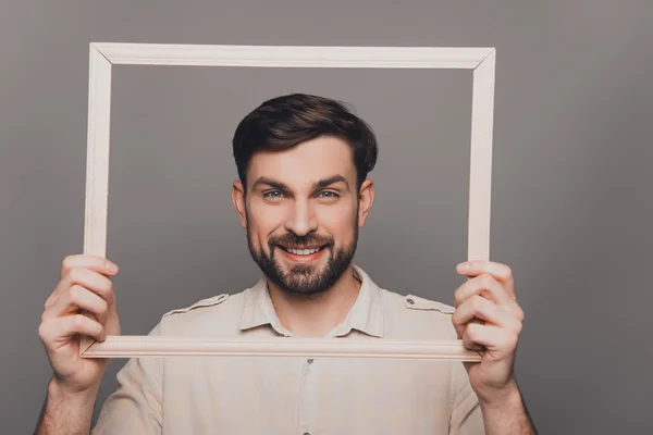 Retrato de hombre barbudo sonriente feliz sosteniendo marco de madera —  Fotos de Stock