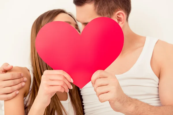 Retrato de cerca del hombre y la mujer besándose detrás del corazón de papel — Foto de Stock