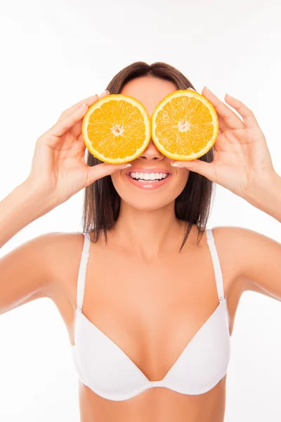 Mujer sonriente cómica en sujetador blanco sosteniendo dos mitades de naranja ne — Foto de Stock