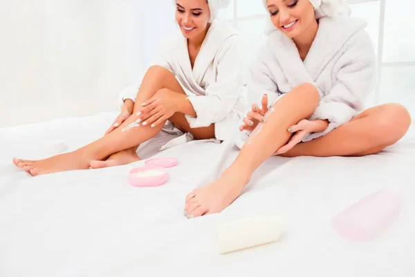 Portrait of two happy smiling girls applying cream on their legs — Stock Photo, Image