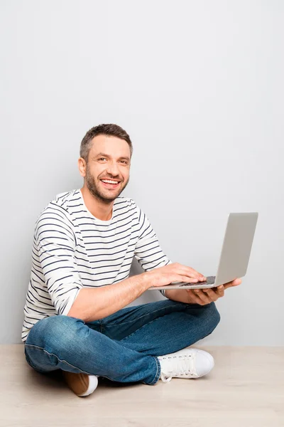 Vrolijke gelukkig Glimlachende man zittend op de vloer met laptop — Stockfoto