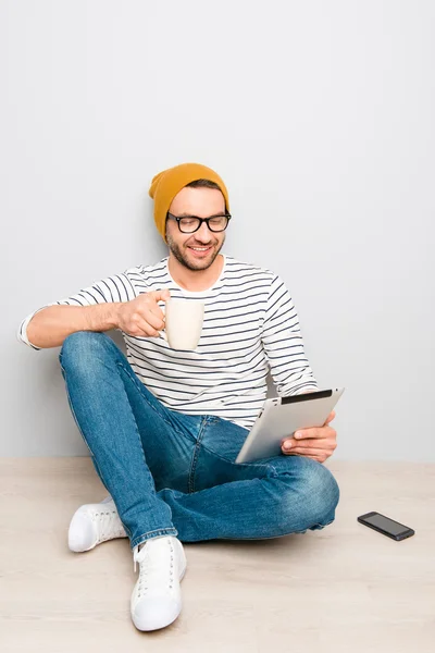 Cara feliz em chapéu e óculos usando tablet e beber café — Fotografia de Stock