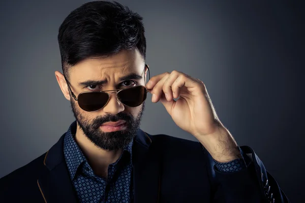 Serious young businessman in suit touching his glasses — Stock Photo, Image