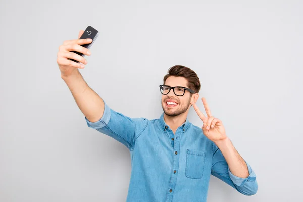 Happy man in glasses making selfie on smartphone and showing two — Stock Photo, Image