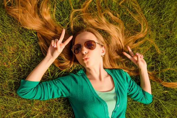 Young girl pouting and gesturing with two fingers while lying on — Stock Photo, Image