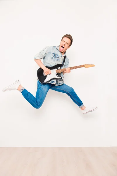 Jovem roqueiro tocando na guitarra electro, mostrando língua e salto — Fotografia de Stock