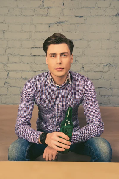 Portrait of handsome young man holding bottle of beer and watchi — Stock Photo, Image