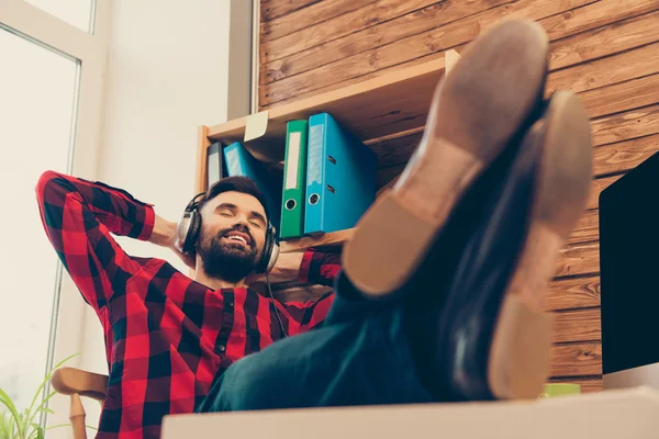 Joven hombre relajado escuchando música y sosteniendo las piernas en la mesa — Foto de Stock