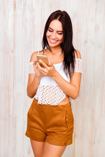 Alegre de moda joven morena escribiendo SMS en el teléfono inteligente — Foto de Stock