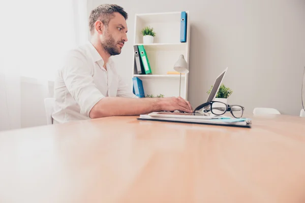 Hombre barbudo guapo haciendo trabajo y escribiendo en el ordenador portátil — Foto de Stock