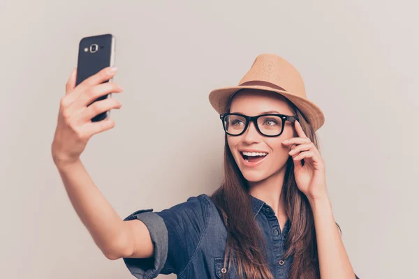 Веселая девушка в кепке и очках делает селфи на смартфоне — стоковое фото