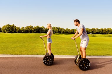 Happy young couple having date and riding segway in park clipart